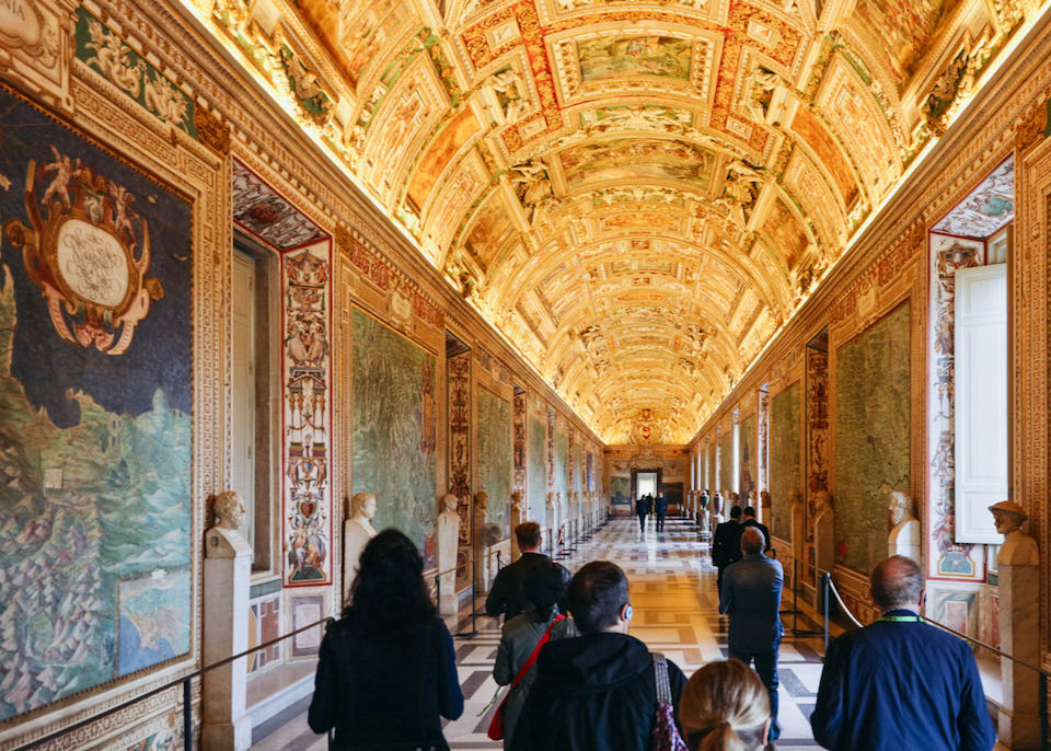 A tour group walks down a beautiful hallway lined with murals in the Vatican Museums.