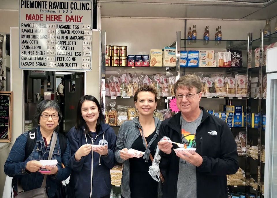 People on a food tour pose with samples in an Italian food shop and ravioli bakery