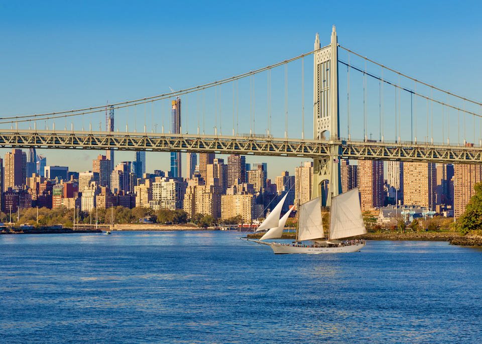 A schooner sails near the RFK Triborough Bridge with Manhattan Midtown an Upper East side Skyscrapers in Background at sunset.