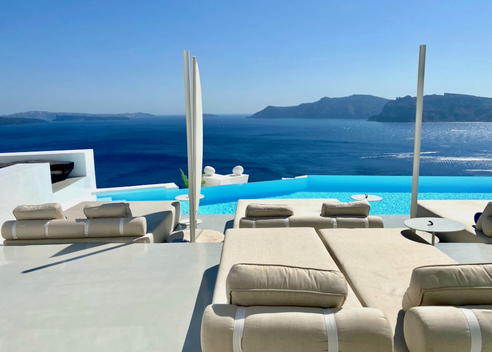 Luxurious upholstered sun loungers in front of an infinity pool overlooking the sea and Santorini volcano