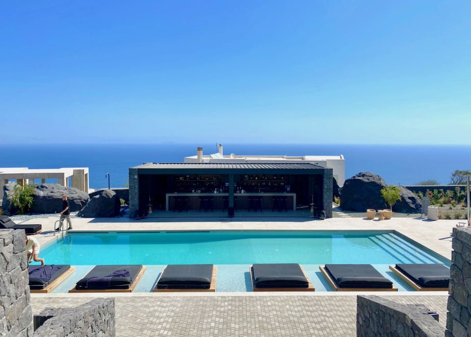 Hotel sun deck with views over the Aegean and a blue swimming pool flanked by sun loungers and a pool bar