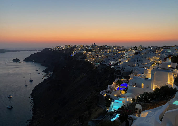 View of the cliffs of Oia, with hotels and restaurants lit up at sunset.