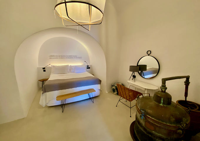 Hotel bedroom with coved, Cycladic ceilings, a dressing table, and an antique wine press