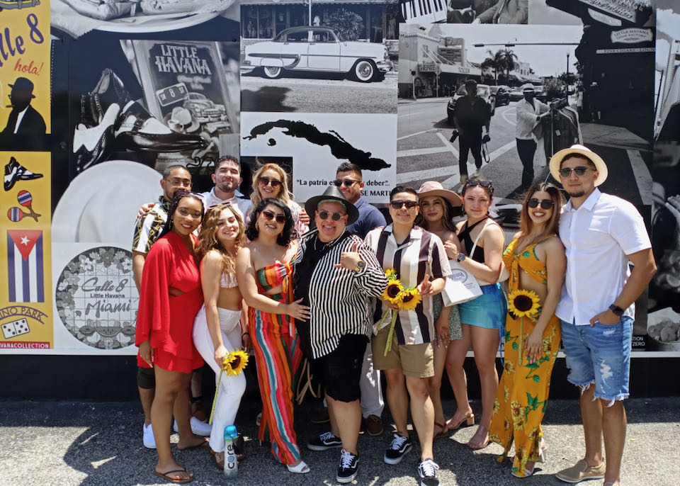 A smiling tour group poses for a photo in front of a mural in Little Havana, Miami 