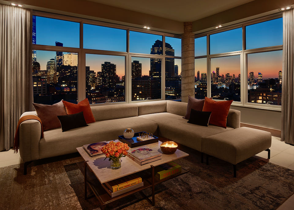 Penthouse living room with plush sectional sofa against a bank of large windows with a view of Manhattan at dusk