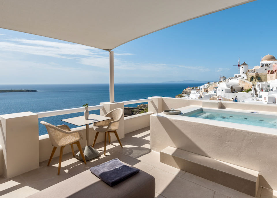 Hotel balcony overlooking the cliffs of Oia and the Aegean Sea with a private plunge pool and cafe table for two.