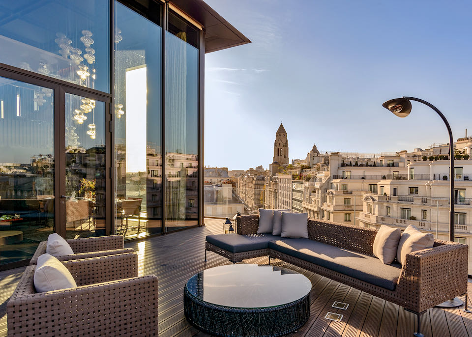 A furnished terrace overlooking Parisian rooftops, opening to a glassed-in dining room with blown-glass chandelier.