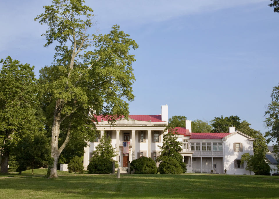 A white, red-roofed, plantation house sits on a large green lawn.