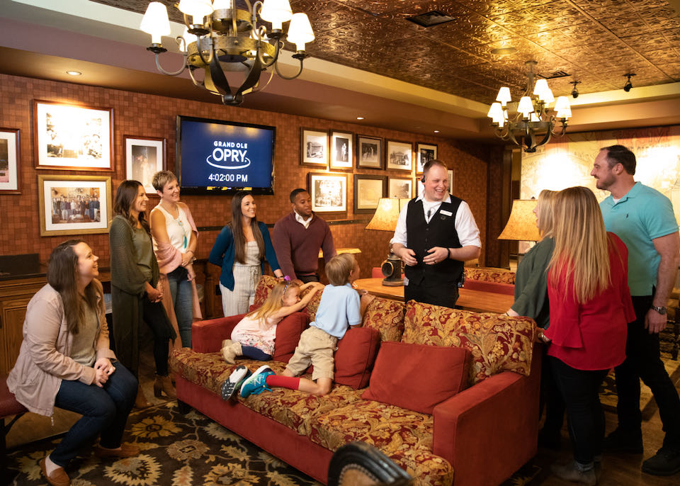 A tour guide talks to a group of smiling tourists inside of a plush dressing room at the Grand Old Opry House