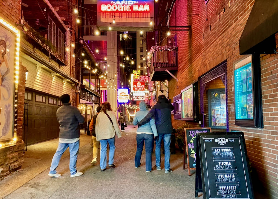 A group of tourists walk down an alley covered with neon signs at night