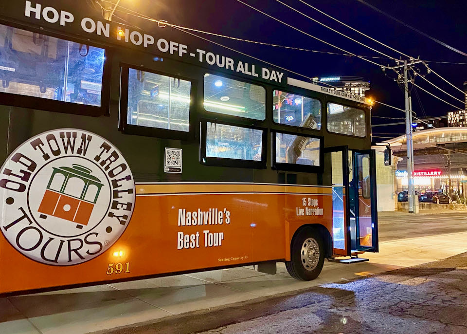 A hop-on tour trolley tour bus at night, in front of a distillery