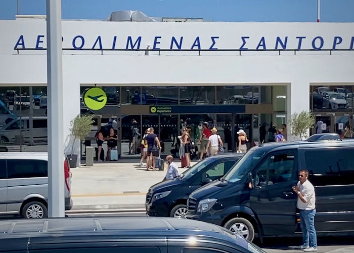 Line of departing travelers at the Santorini Airport, extending out the door and down the sidewalk
