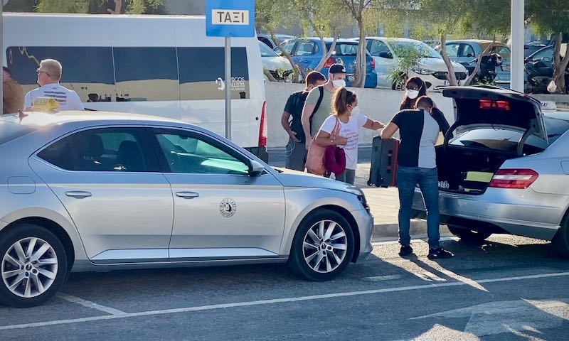 Travelers load their suitcases into the back of a taxi at the Santorini airport
