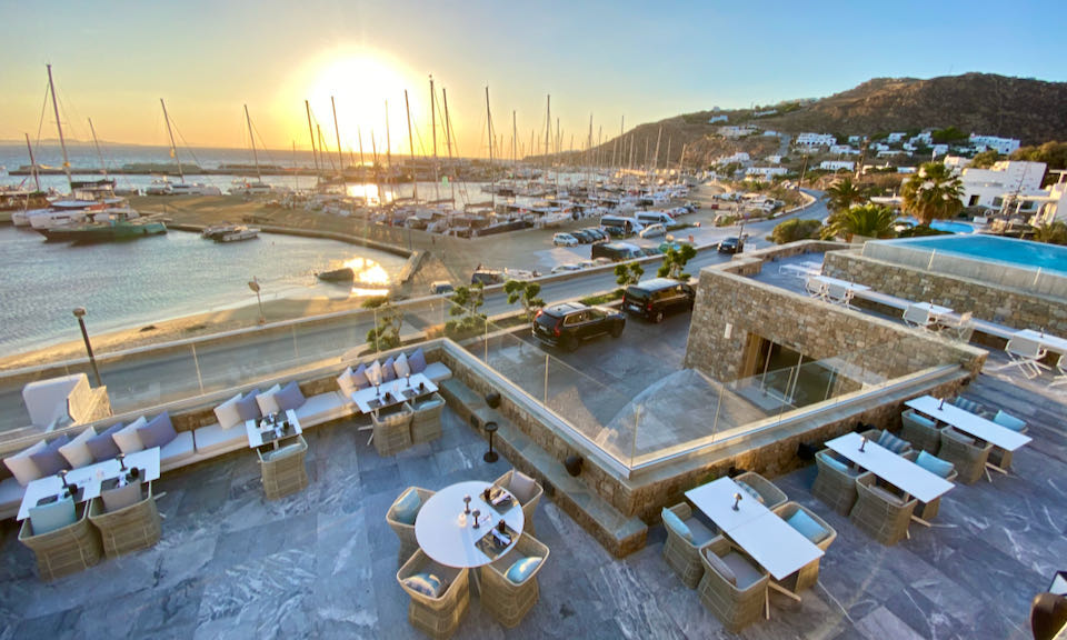 A hotel restaurant with adjacent swimming pool, overlooking a marina filled with sailing yachts.