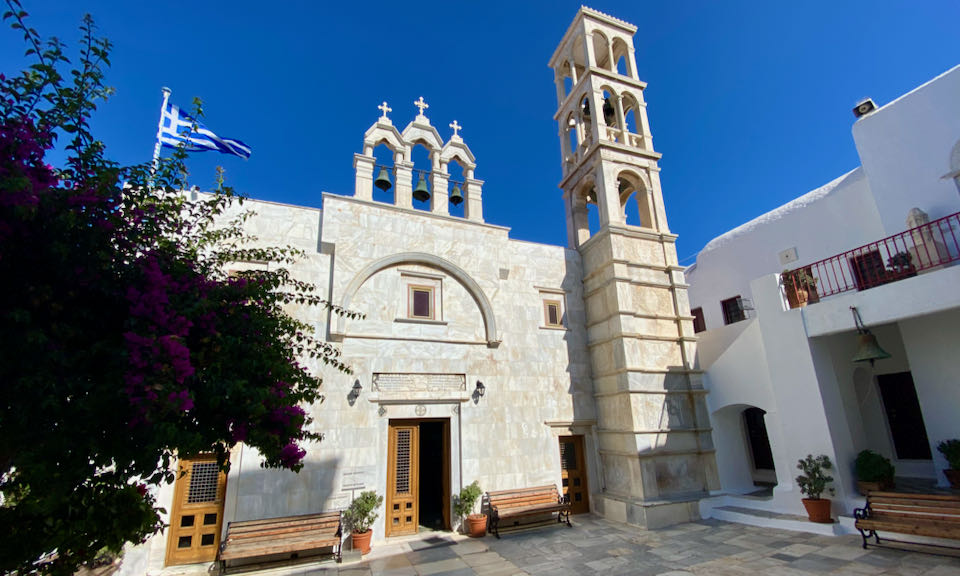 A white monastery with belltower, flying a Greek flag