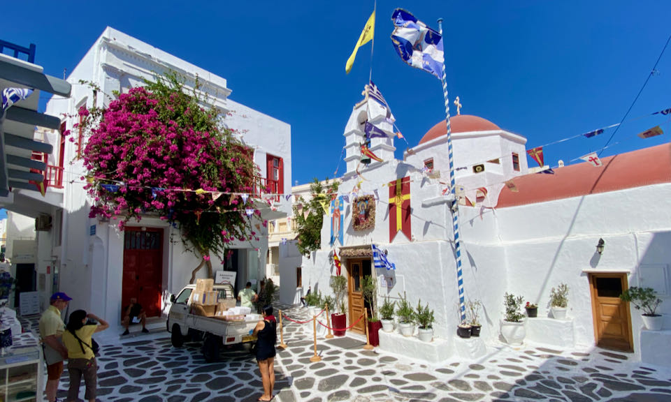A white, red-domed church festooned with Greek flags in a cobblestone square