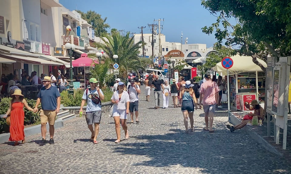 Tourists walk along a cobbled street lined with restaurants and other businesses