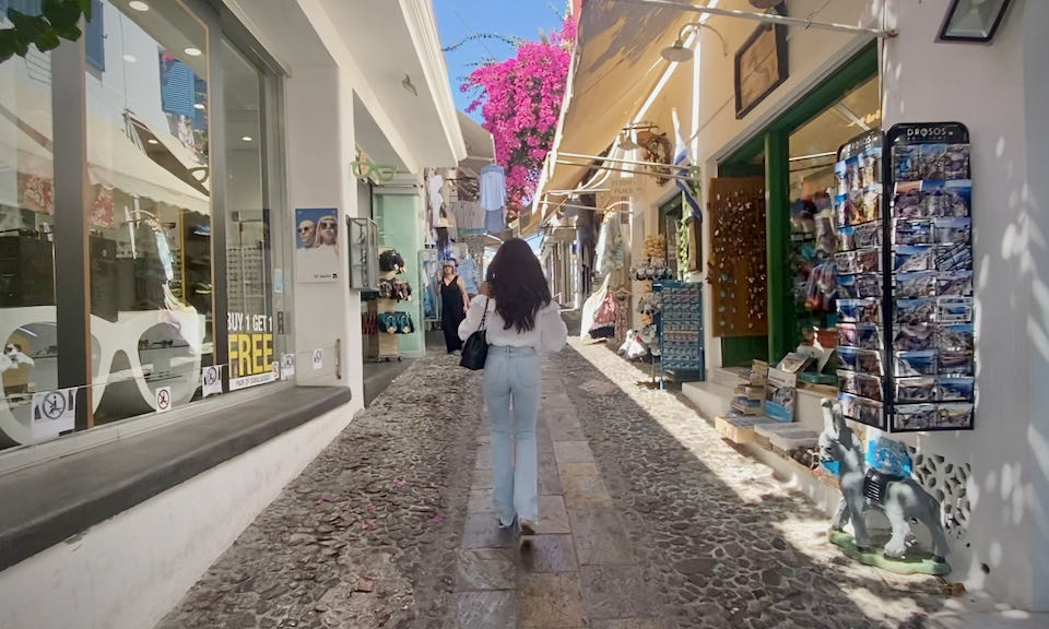 A woman walks along a cobblestone path lined with tourist shops.