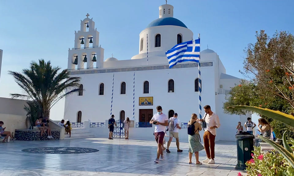 White Greek Orthodox church with a blue dome on a marble plaza