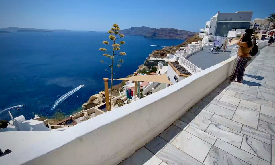 A woman takes a photo of the Santorini caldera from a marble footpath
