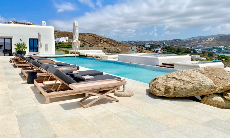 Rectangular blue pool surrounded by sun loungers on a smooth concrete terrace.