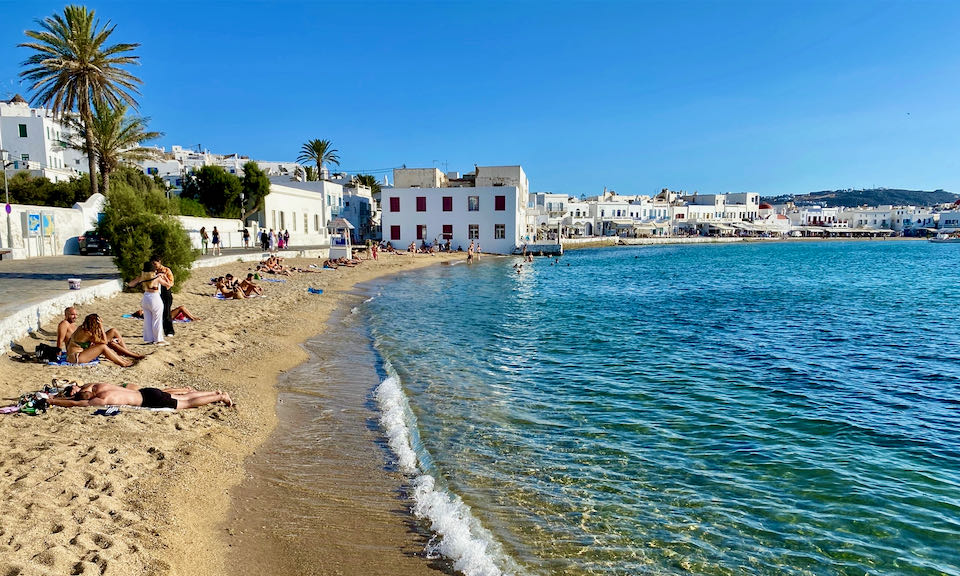 Sandy beach at the edge of a Greek village with white boxy buildings