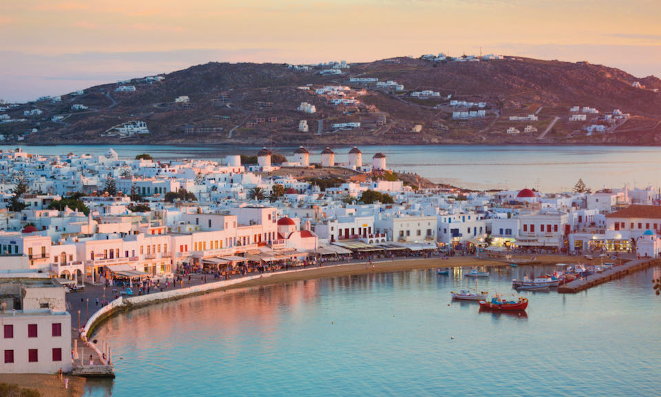 Aerial view of the buildings along Mykonos Town harbor, with the famous windmills in the background.