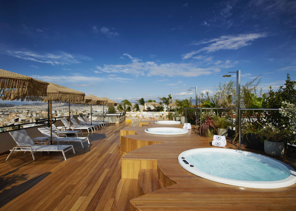 Rooftop sundeck with lounge chairs, wooden decking, and multiple hot tubs.