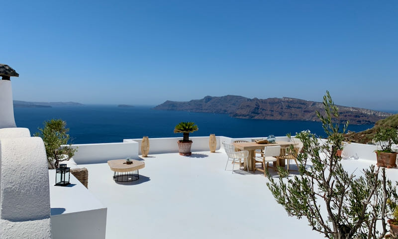 A white hotel veranda overlooking the blue sea and steep cliffs of Santorini