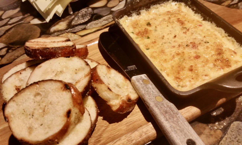 A small pan of roasted cheese dip with a side of toasted bread rounds