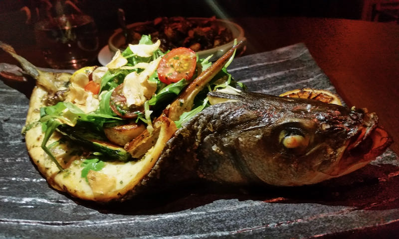 A whole fried fish with back cavity split open and filled with vegetables.
