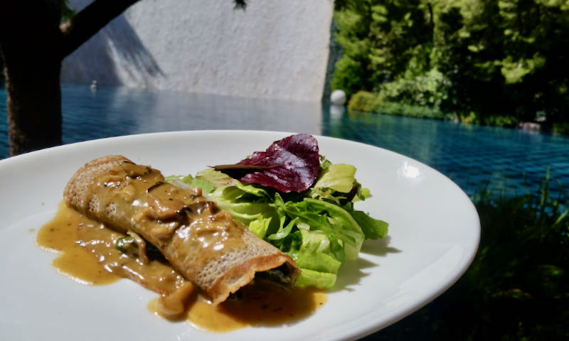 A buckwheat crepe, served next to a mixed green salad and drizzled with sauce.