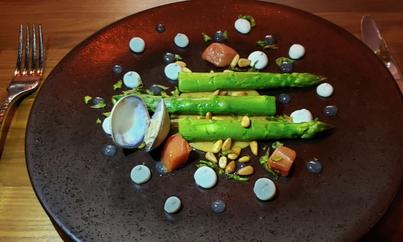 Asparagus spears, a clam, and bites of raw tuna are arranged artfully on a plate, and decorated with dots of sauce.