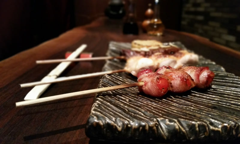 a row of wooden kebab skewers on a small platter, each serving a different type of meat