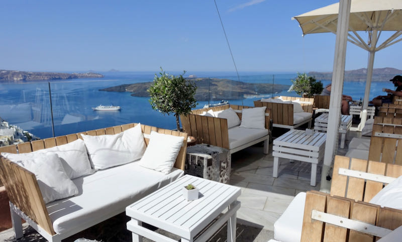 Outdoor tables and couches on a sun seck overlooking the Santorini caldera