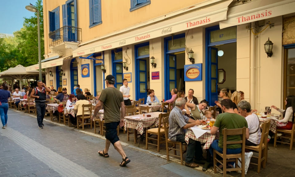 Diners sit at outdoor tables lining a pedestrian alley in Athens.