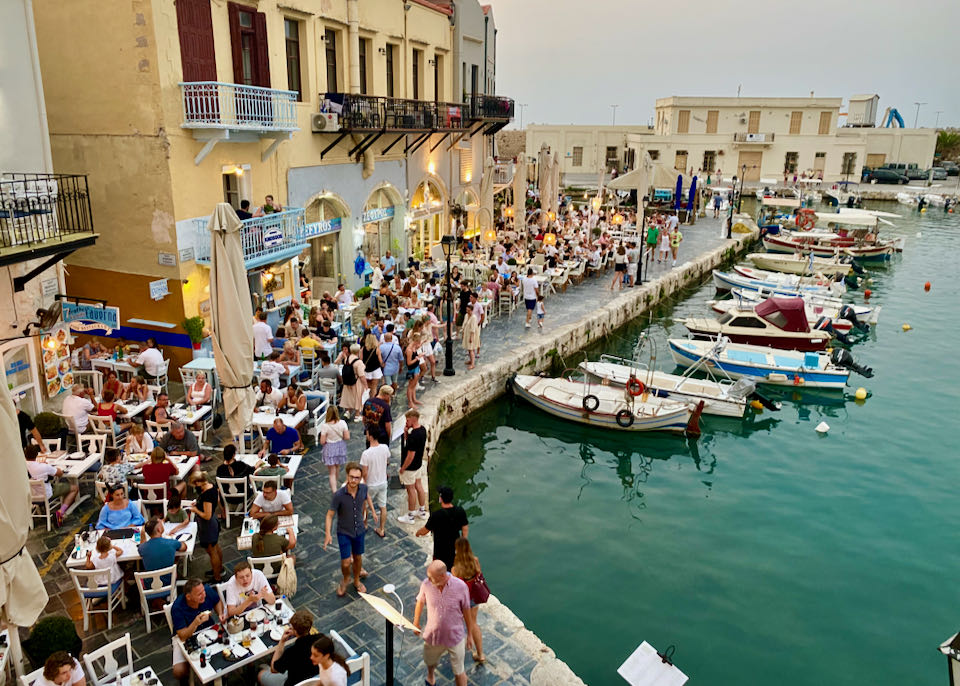 A crowded harbor with pastel-colored buildings and outdoor cafes.