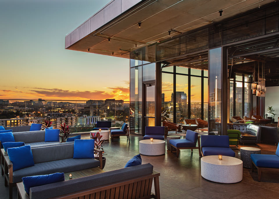 Outdoor rooftop lounge at dusk with sofas, candle-lit tables, and views over downtown Nashville. 