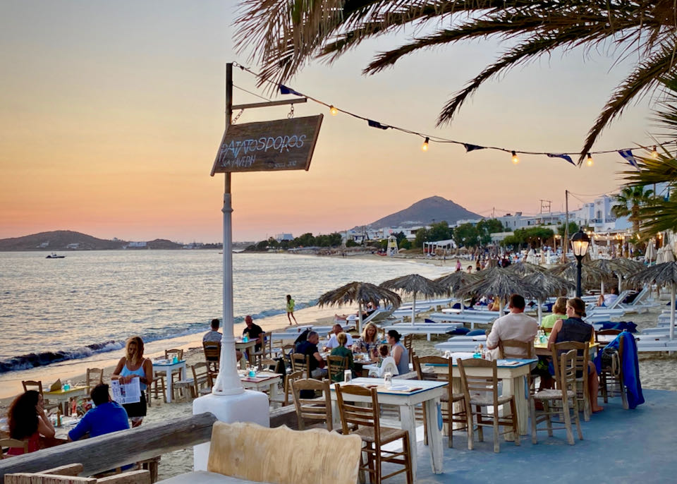 Tables of diners on a beach at sunset, with a mountain in the distance.