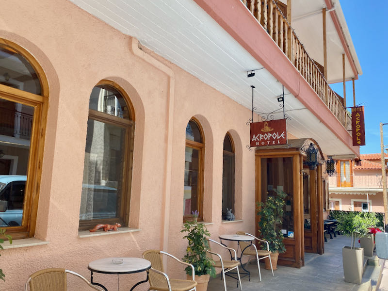 Sidewalk seating and entryway of a pink stucco hotel with brown wooden doorway