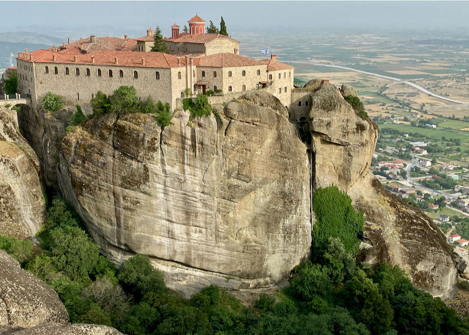A vast stone monastery sits atop a sandstone pillar, high above the ground