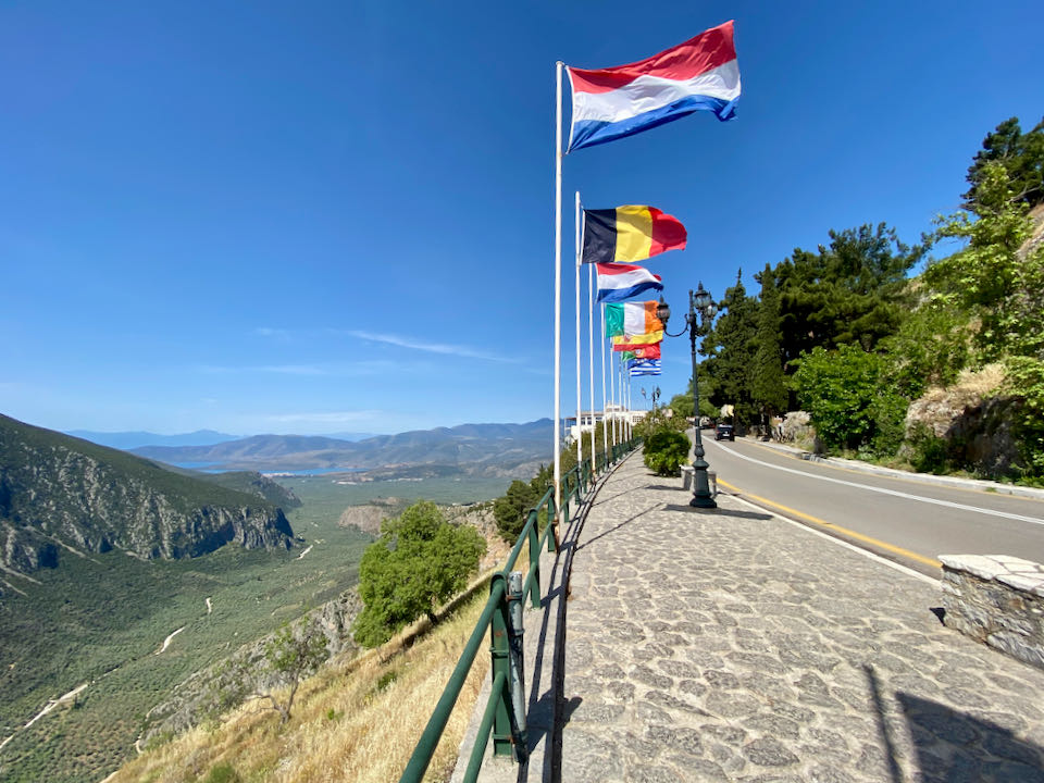 A row of flagpoles flying international flags sits above a beautiful valley.