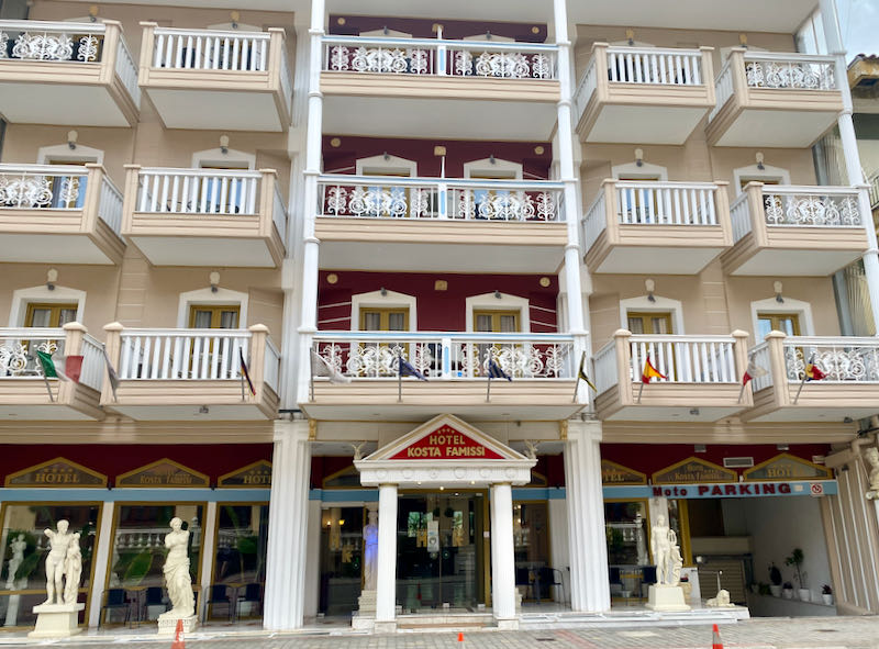 Large hotel with white iron balconies and Greek-style pillars and statues in front