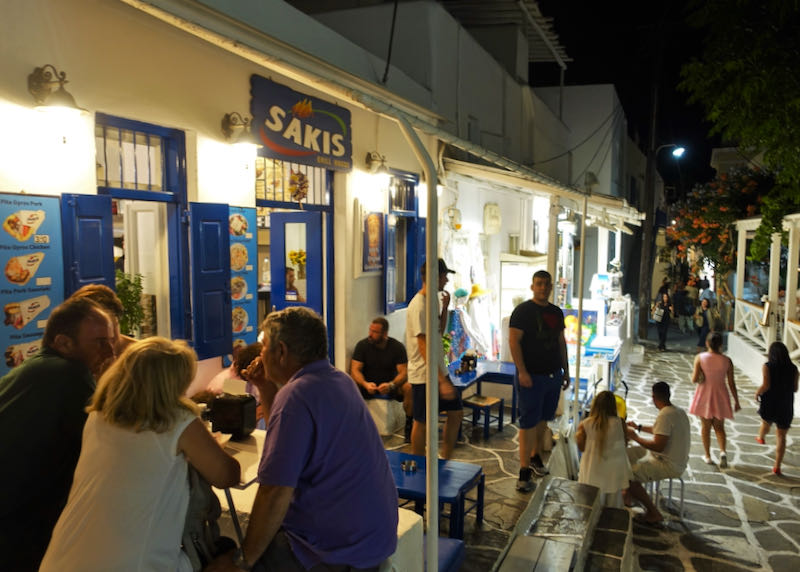 Diners sit at crowded outdoor tables at a souvlaki restaurant at night