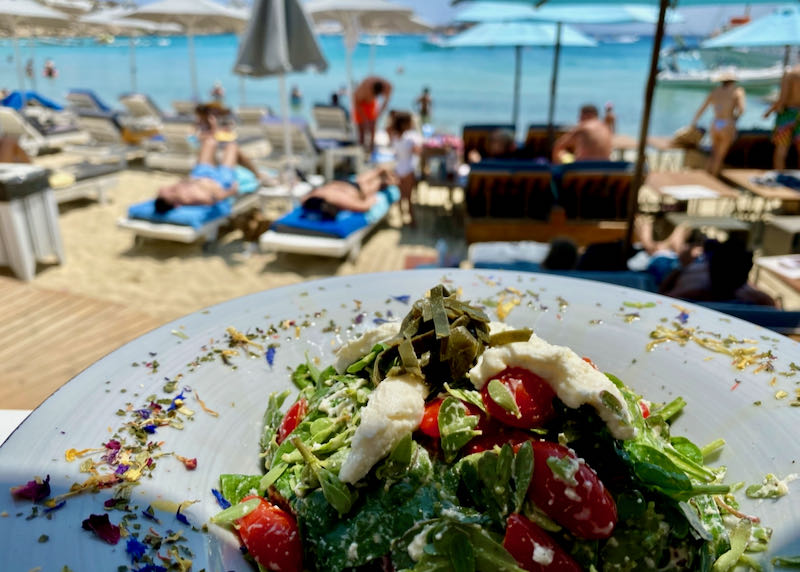 View over a Greek salad to a row of sunbeds on a sandy beach
