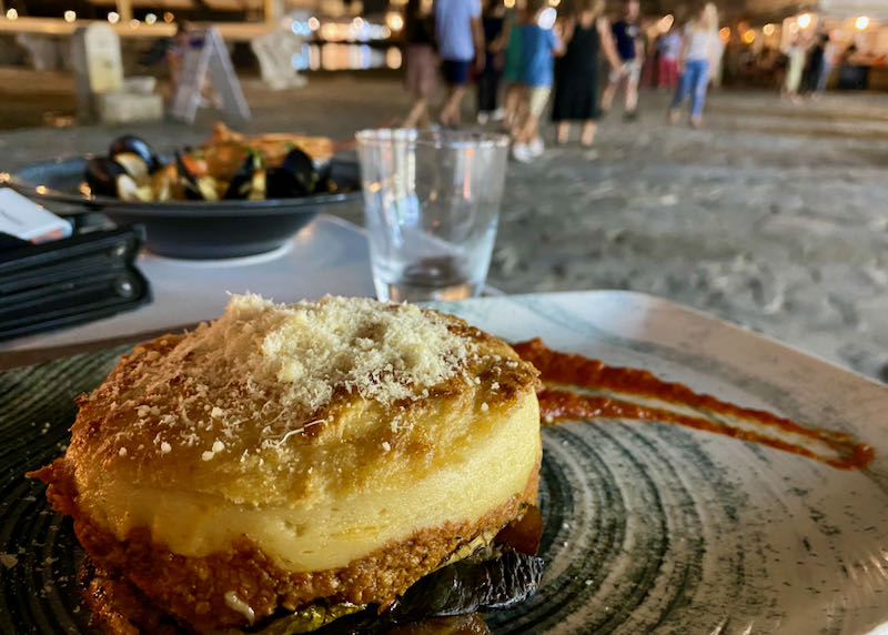 View across a plate of pastitsio to a cobbled plaza