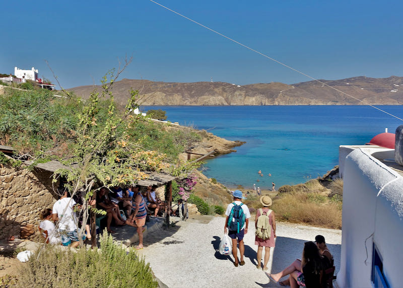 People walk down a sandy path to a rustic restaurant overlooking the beach