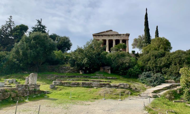 View of an ancient Greek temple from below, surrounded by greenery