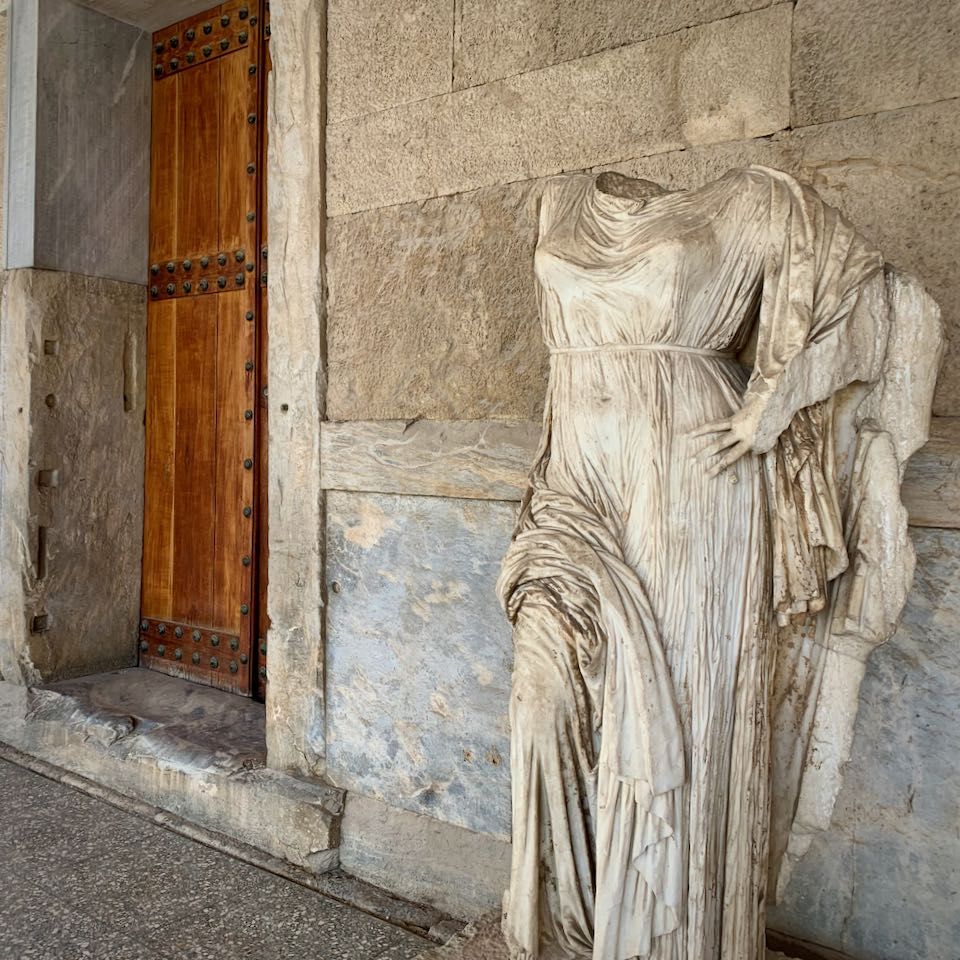 Statue of a robed woman with her hand on her hip. The head is missing.
