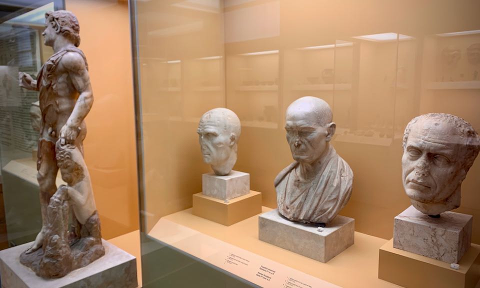 Marble busts and a statue of a dancing man in museum displays